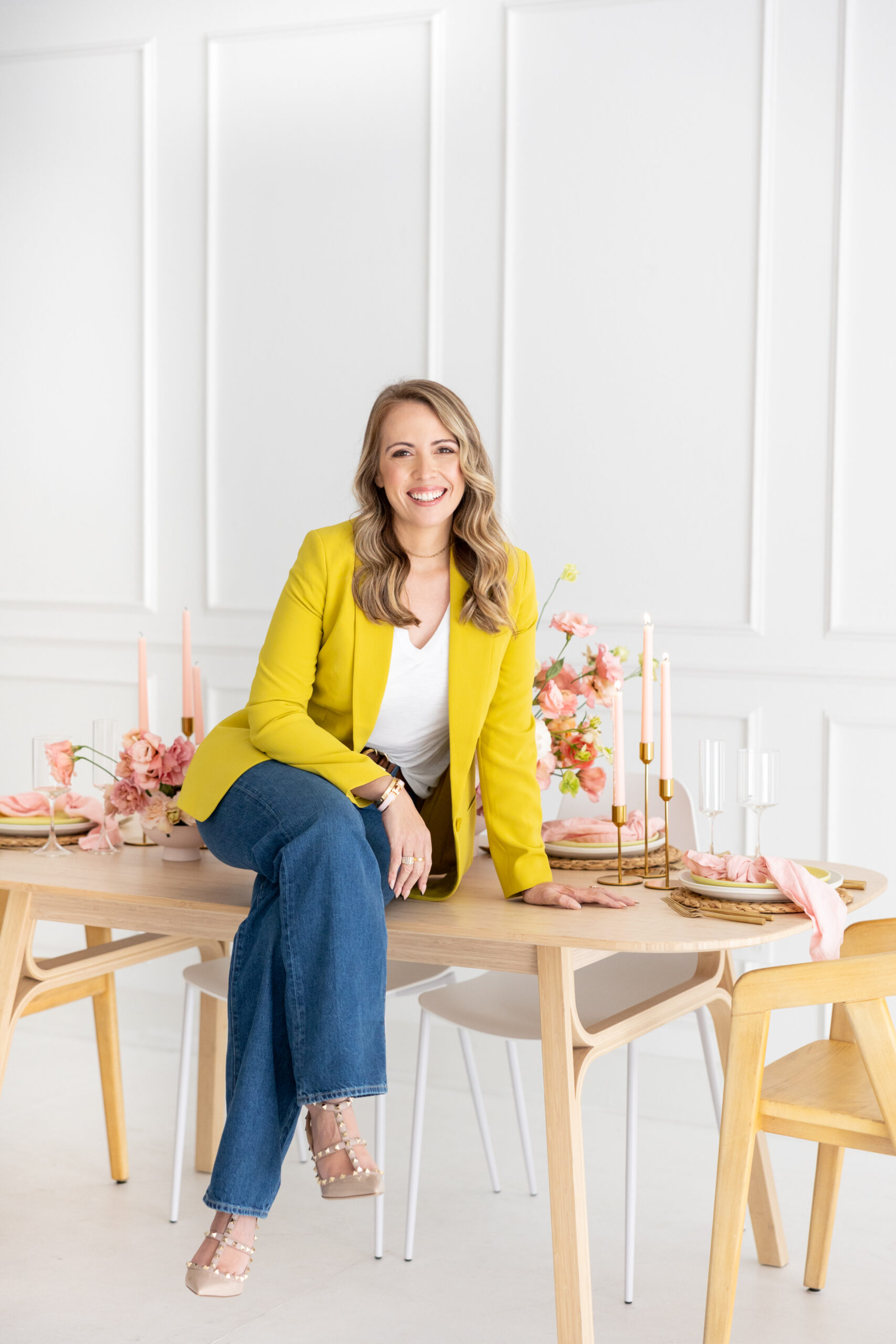 A woman in a yellow jacket participating in a brand photoshoot as a wedding planner at a wooden table.