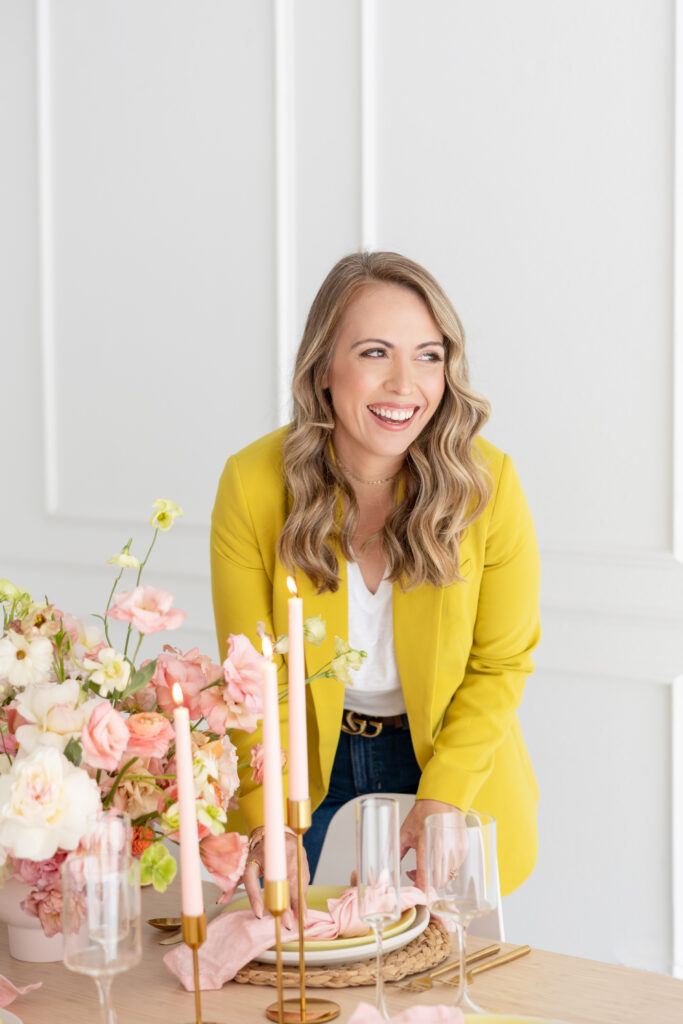 A woman in a yellow jacket standing at a table with pink flowers during a brand photoshoot.