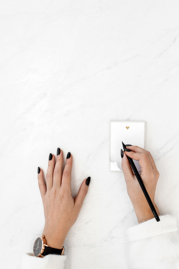 A woman's hands showcasing her core values as she writes on a notepad on a marble table.