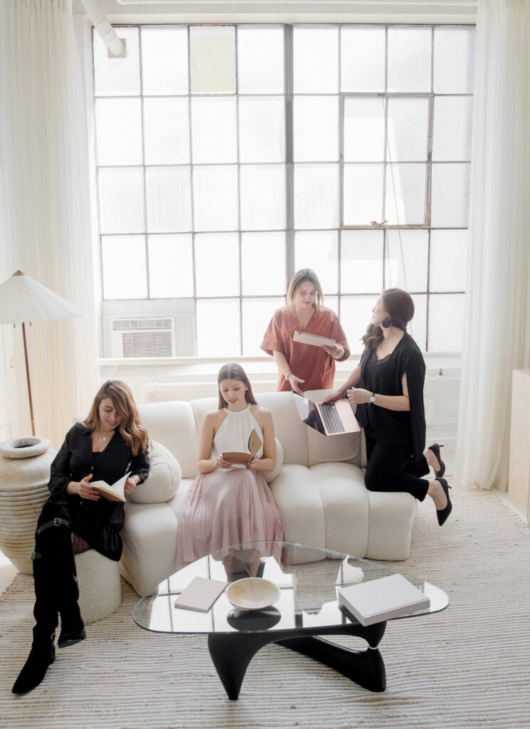 Four women sitting on a white couch in a living room, discussing social media management tools.