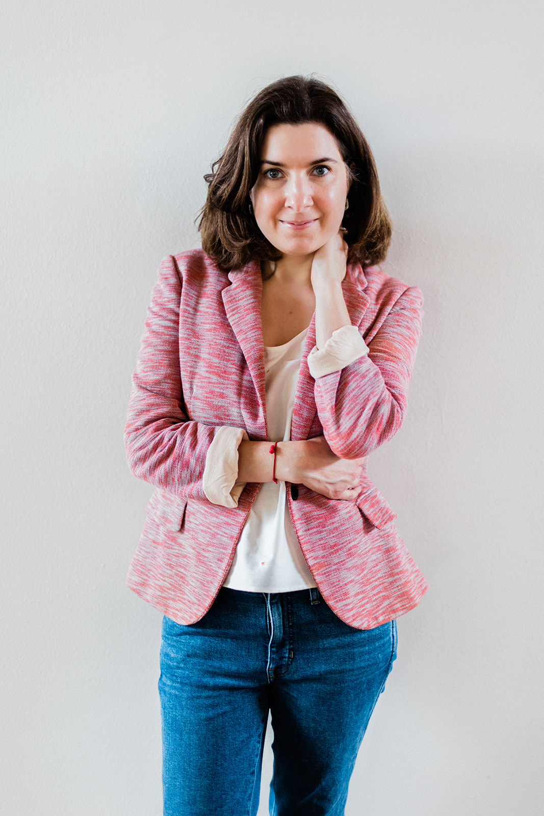 Confident woman in a pink blazer and jeans with her chin resting on her hand, resembling the expertise of Andrea Shah, the wedding website copywriter.