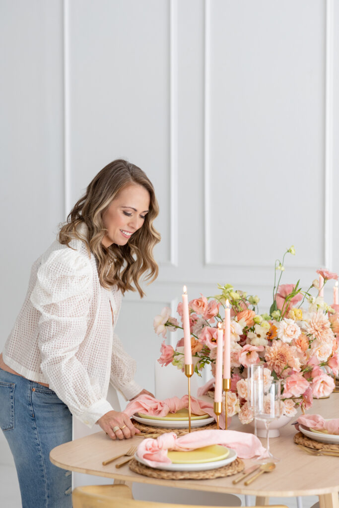 A wedding planner setting a table with pink flowers and candles.
