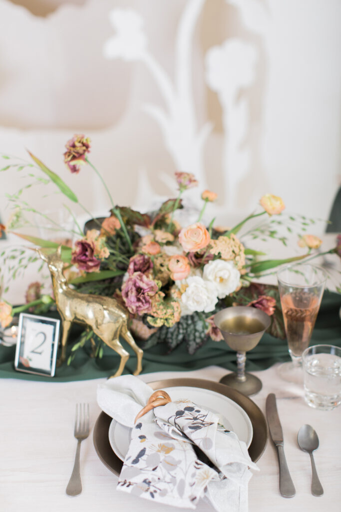A wedding planner process table setting with a gold deer figurine and green flowers.