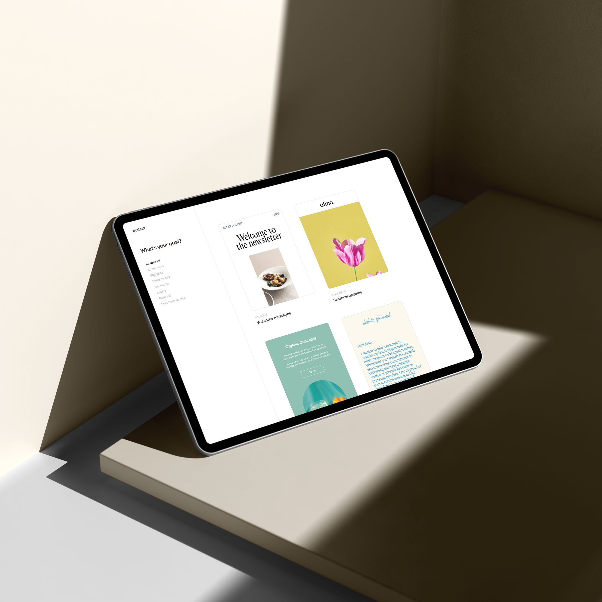 A tablet displaying a design interface with welcome banners and graphics, positioned on a table in a brightly lit room with shadows. Ideal for crafting captivating emails and checking out Flodesk reviews for inspiration.