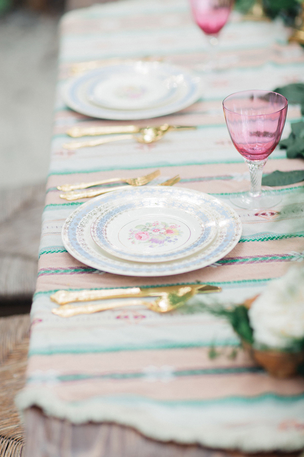 A table set with patterned plates, gold cutlery, and pink wine glasses on a striped tablecloth showcases the meticulous attention to detail ideal for wedding planning.