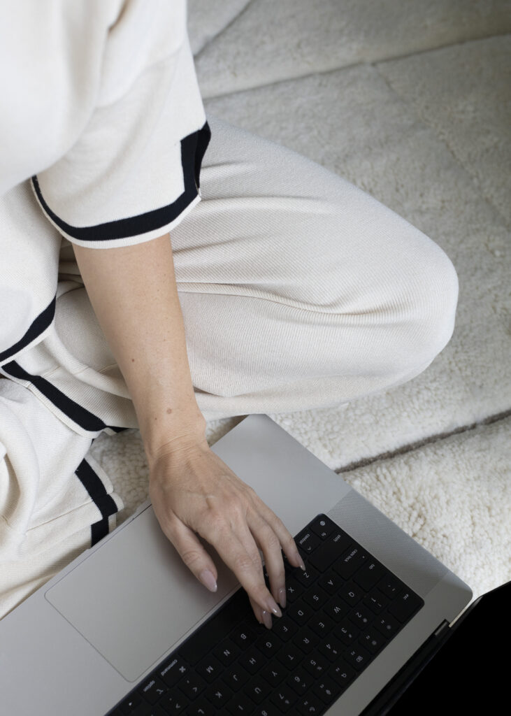 A person in light-colored clothing sits comfortably on a soft surface, exploring free event planning software on their laptop.