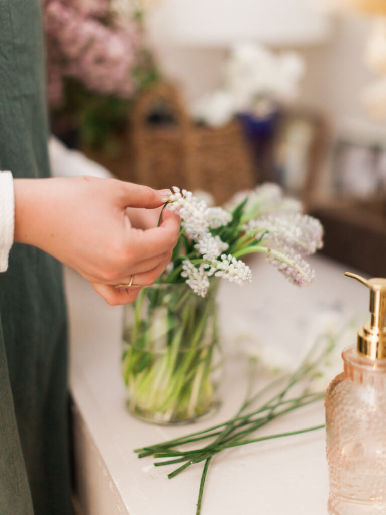 A beginner's guide to floral decor: A person arranges white flowers in a glass jar on a countertop next to a soap dispenser, creating an elegant touch ideal for wedding planners seeking simple yet stunning arrangements.