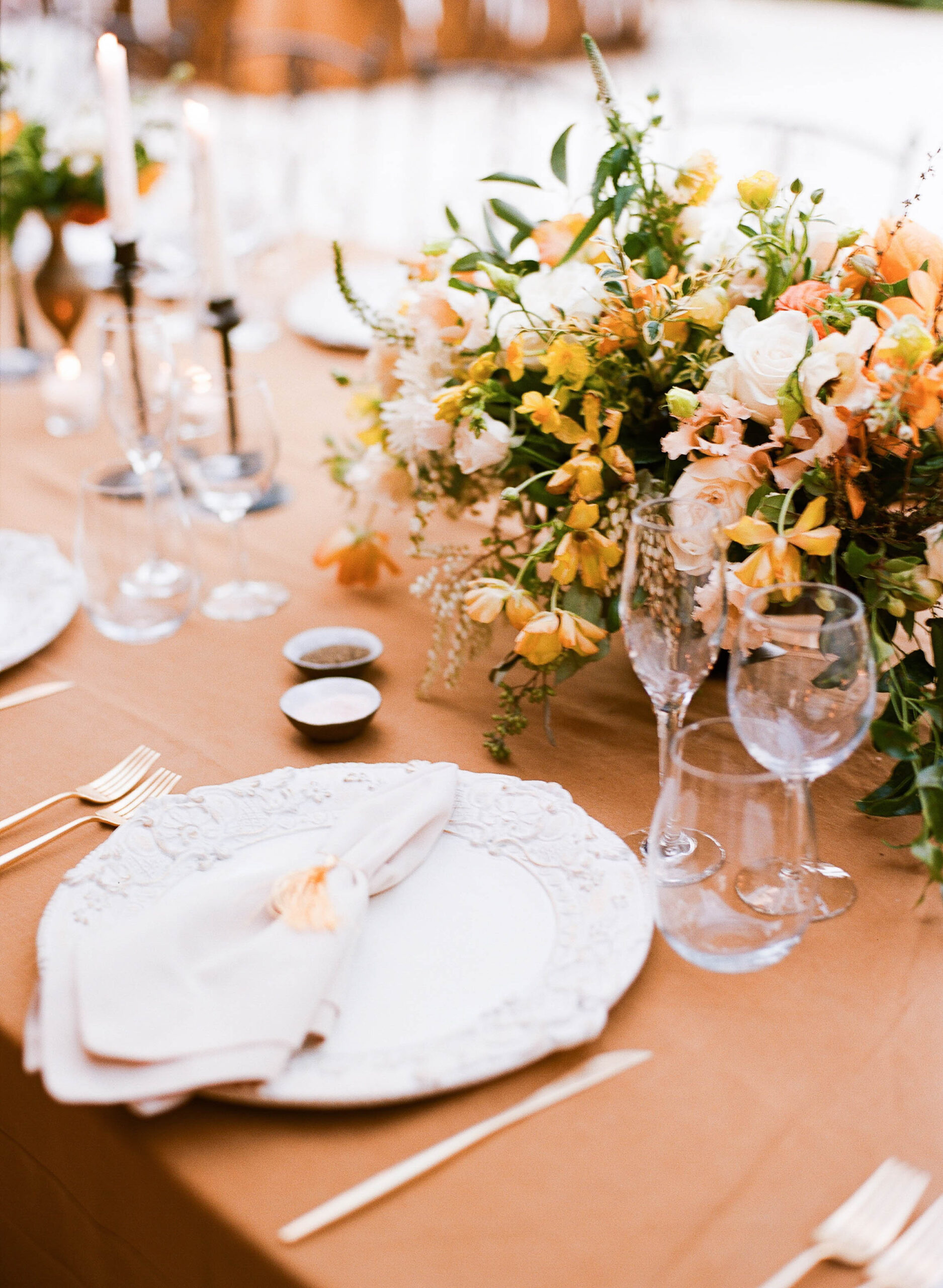 Elegant table setting with ornate white plates, gold cutlery, beige napkins, wine glasses, and a floral centerpiece—showcasing the kind of style that makes it possible to make 100k as a wedding planner.