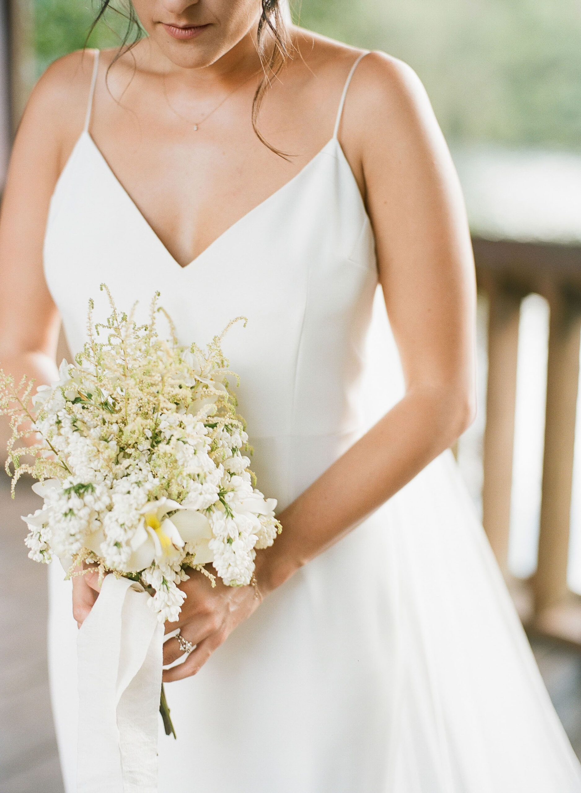 A woman in a sleeveless white wedding dress holds a bouquet of white flowers with greenery and a white ribbon—perfect inspiration for anyone starting a wedding planning business in 2025.