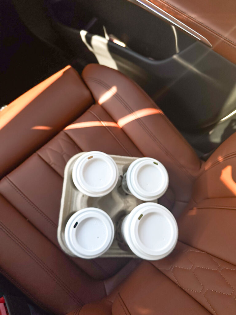 A cardboard drink carrier with four coffee cups sits on the brown leather seat of a car, ready to fuel a team preparing to Train Your Associate Wedding Planners for the big day.