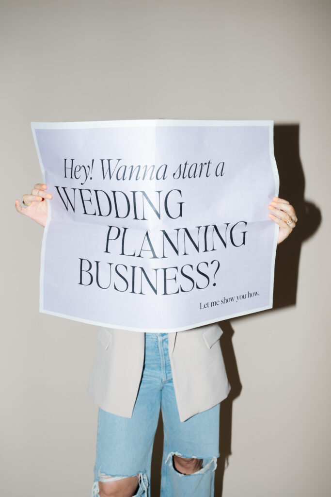 Person holding a large sign that reads, "Hey! Wanna start a WEDDING PLANNING BUSINESS? Let me show you how," perfect for your next brand photoshoot or to boost your wedding planner brand photography content.